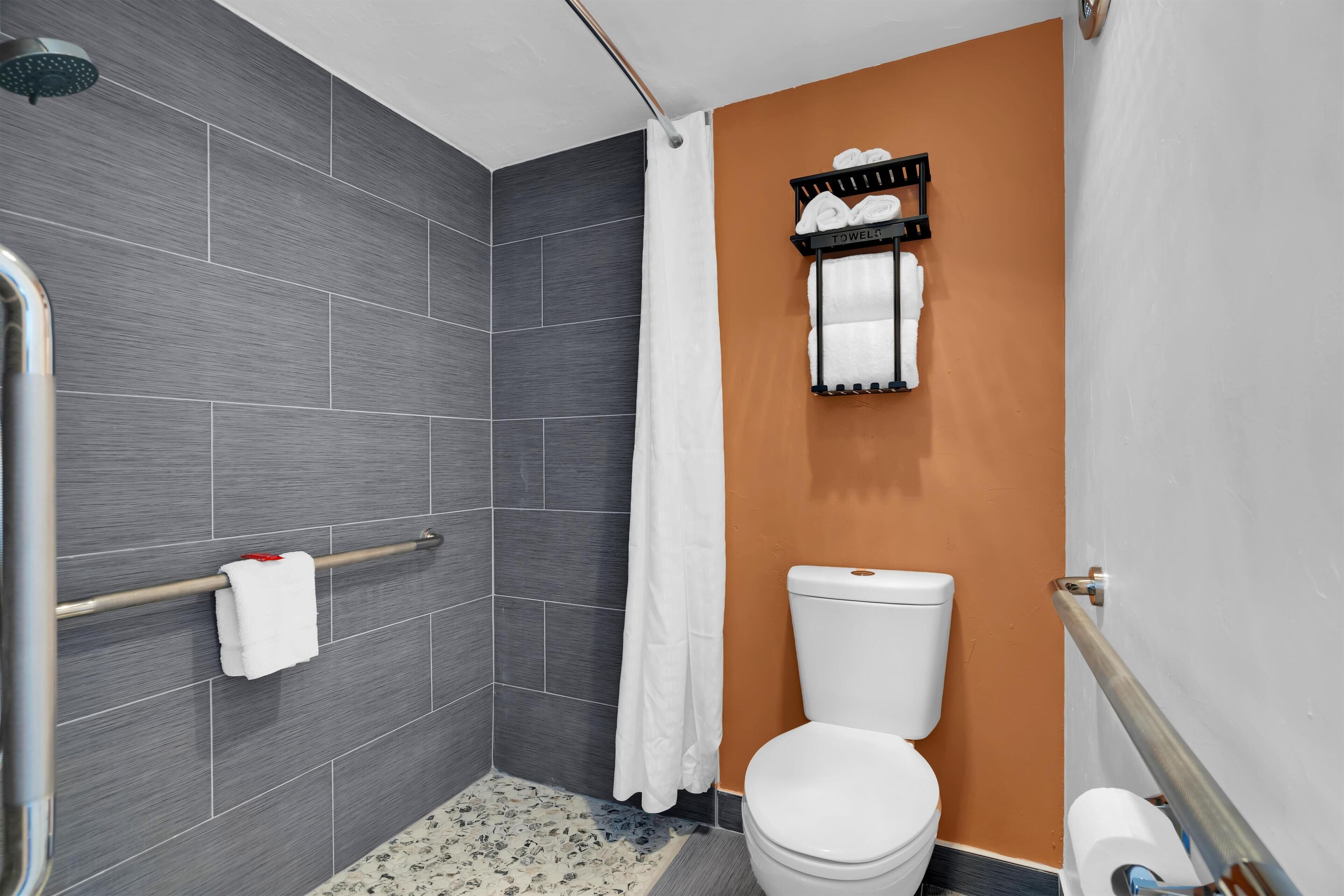 Un baño con ducha, inodoro, tendedero para toallas y dispensador de toallas mural.