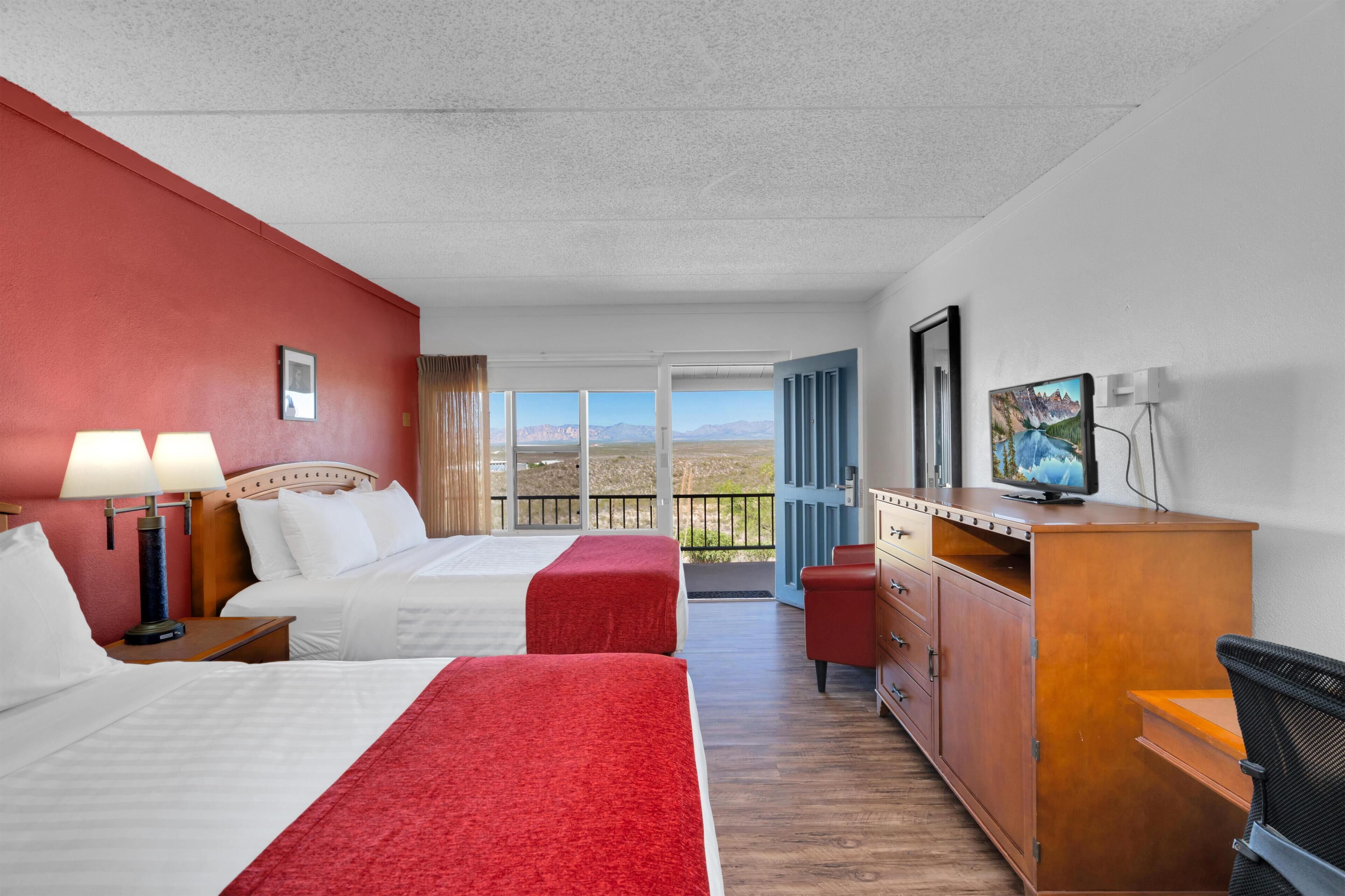 Ein Hotelzimmer mit zwei Betten, einem Schreibtisch, einem Fernseher und einem Balkon mit Bergblick.