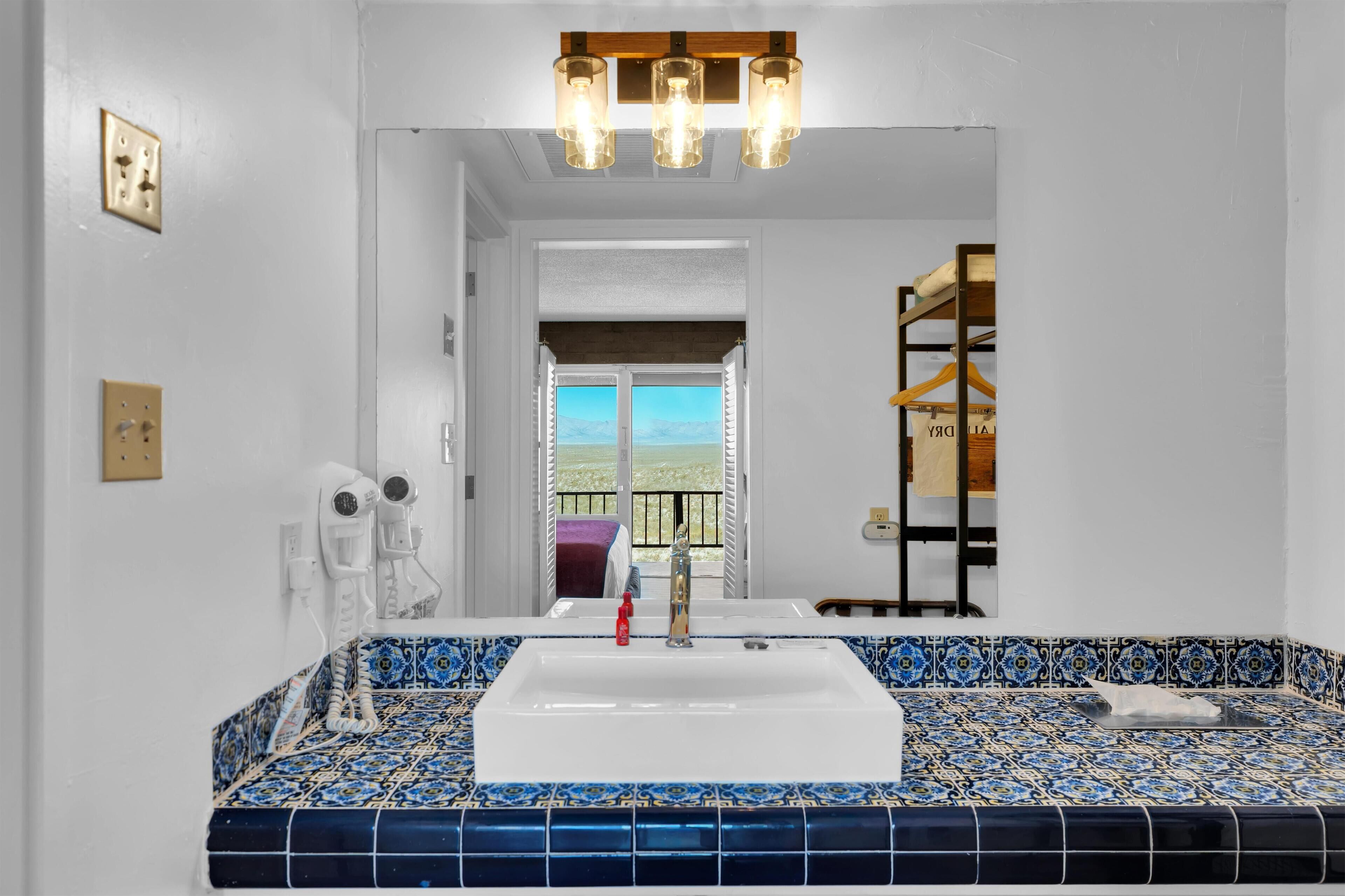 A bathroom with a large sink, a mirror, and a view of the balcony.