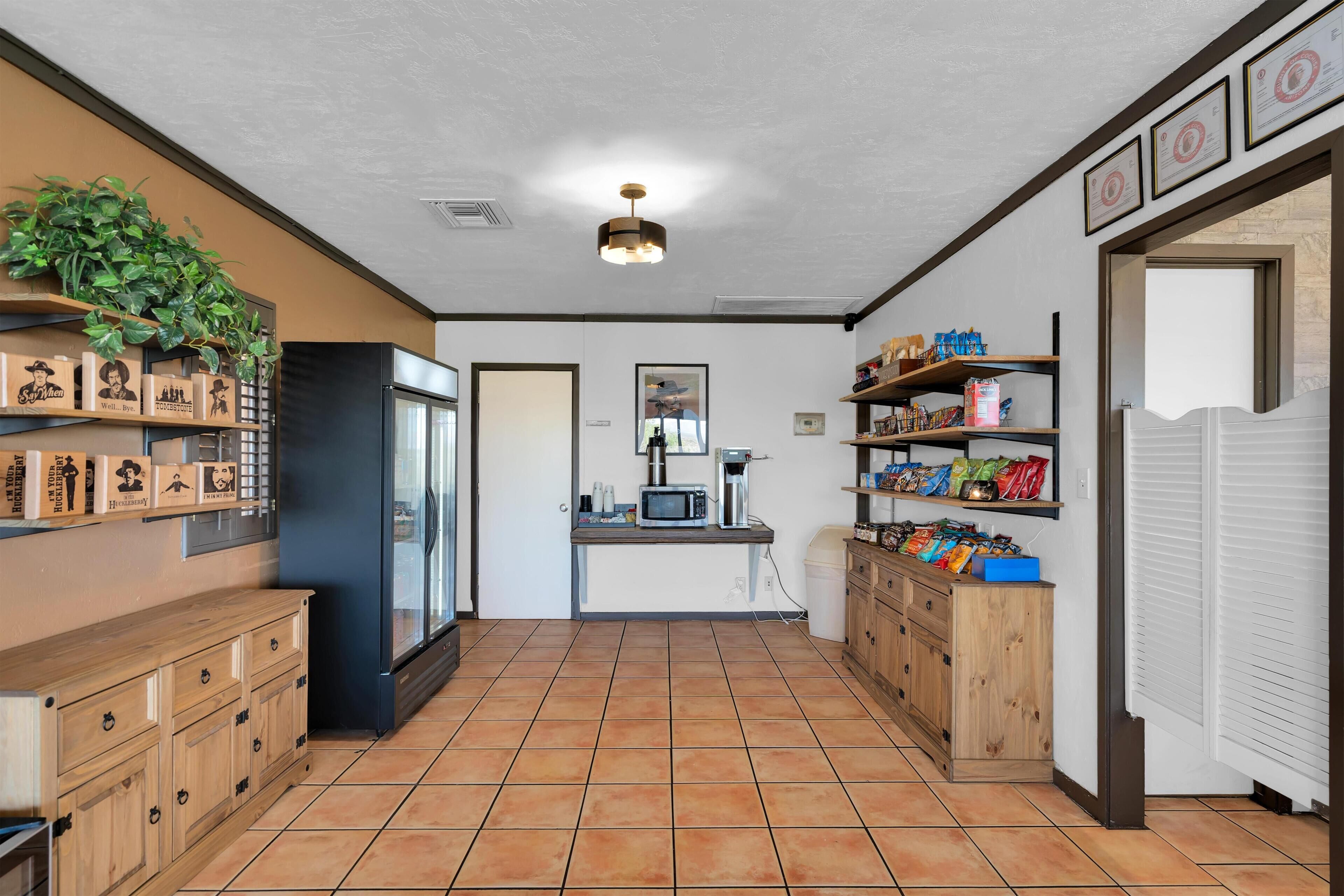 A kitchen with a refrigerator, microwave, and shelves with snacks.