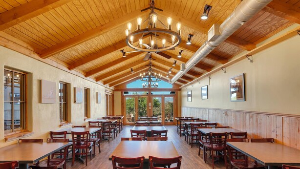 A spacious dining area with wooden tables and chairs, a high wooden ceiling with exposed beams, and large windows allowing natural light. - Tombstone Lookout Lodge, SureStay Collection by Best Western (Tombstone)