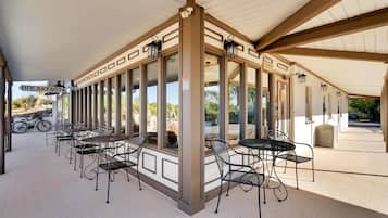A covered outdoor seating area with tables and chairs, a sign for breakfast, and a view of the surrounding landscape.