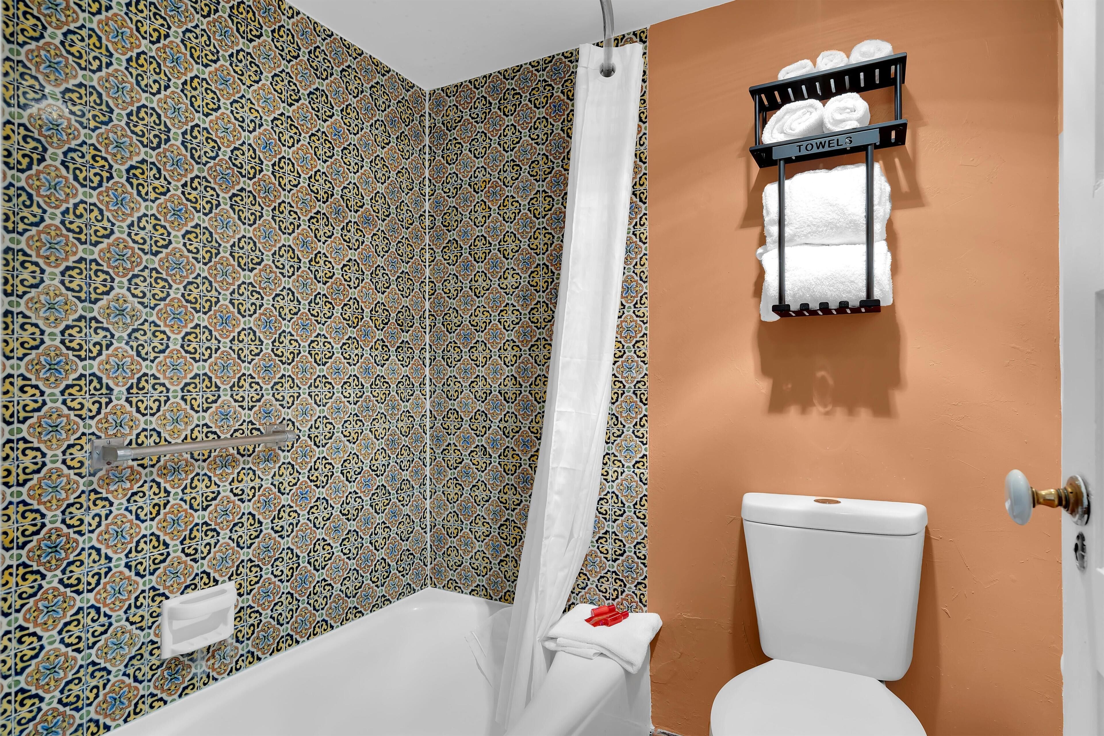Een badkamer met patroontegels, een witte badkuip, een toilet en een handdoekrek met handdoeken.