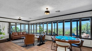 A spacious room with a large window, a brown leather sofa, a poker table, and a dining table with chairs. - Tombstone Lookout Lodge, SureStay Collection by Best Western (Tombstone)