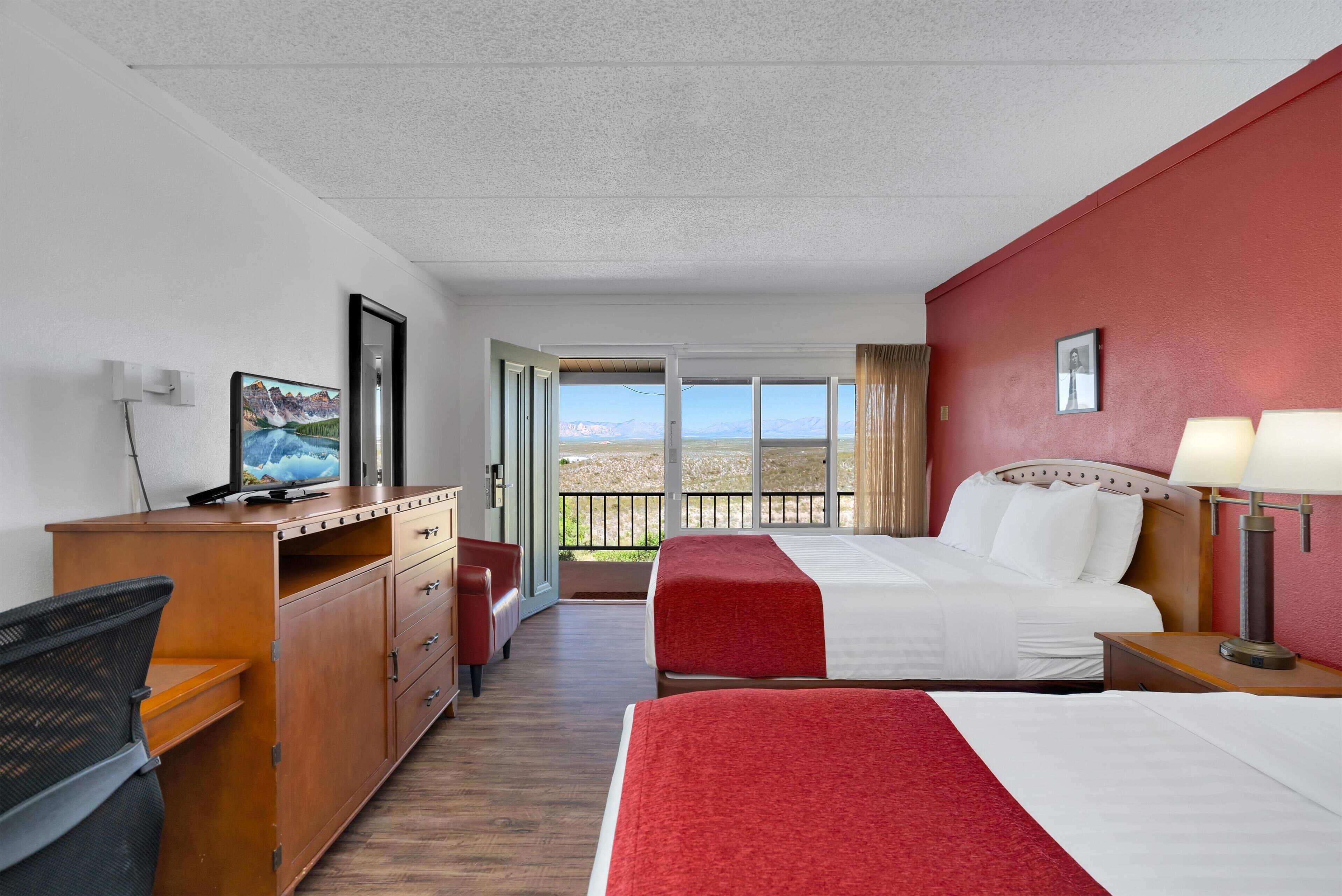 A hotel room with a bed, a desk, a chair, a television, and a balcony with a view.