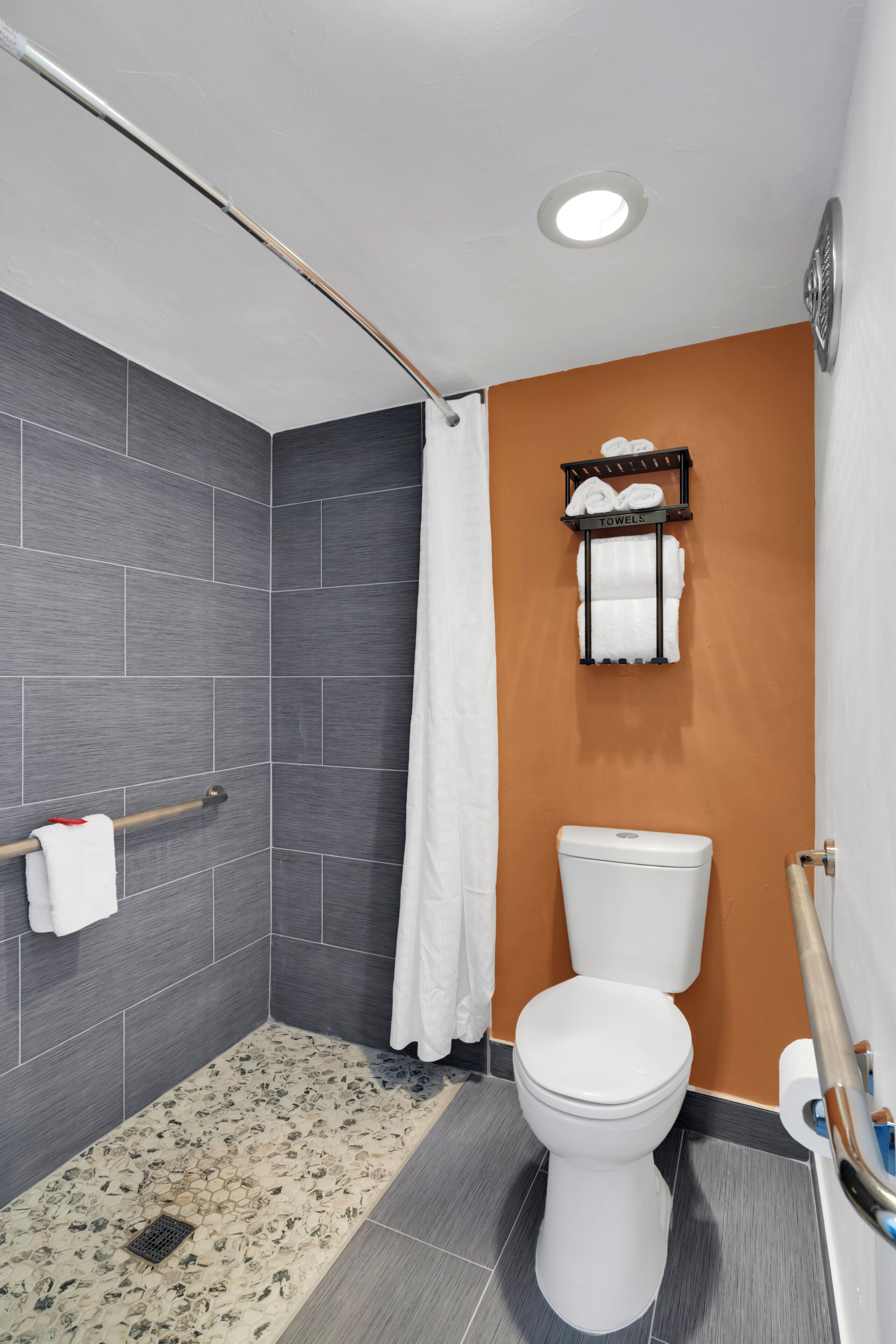 A bathroom with a shower, toilet, towel rack, and a wall-mounted towel dispenser.