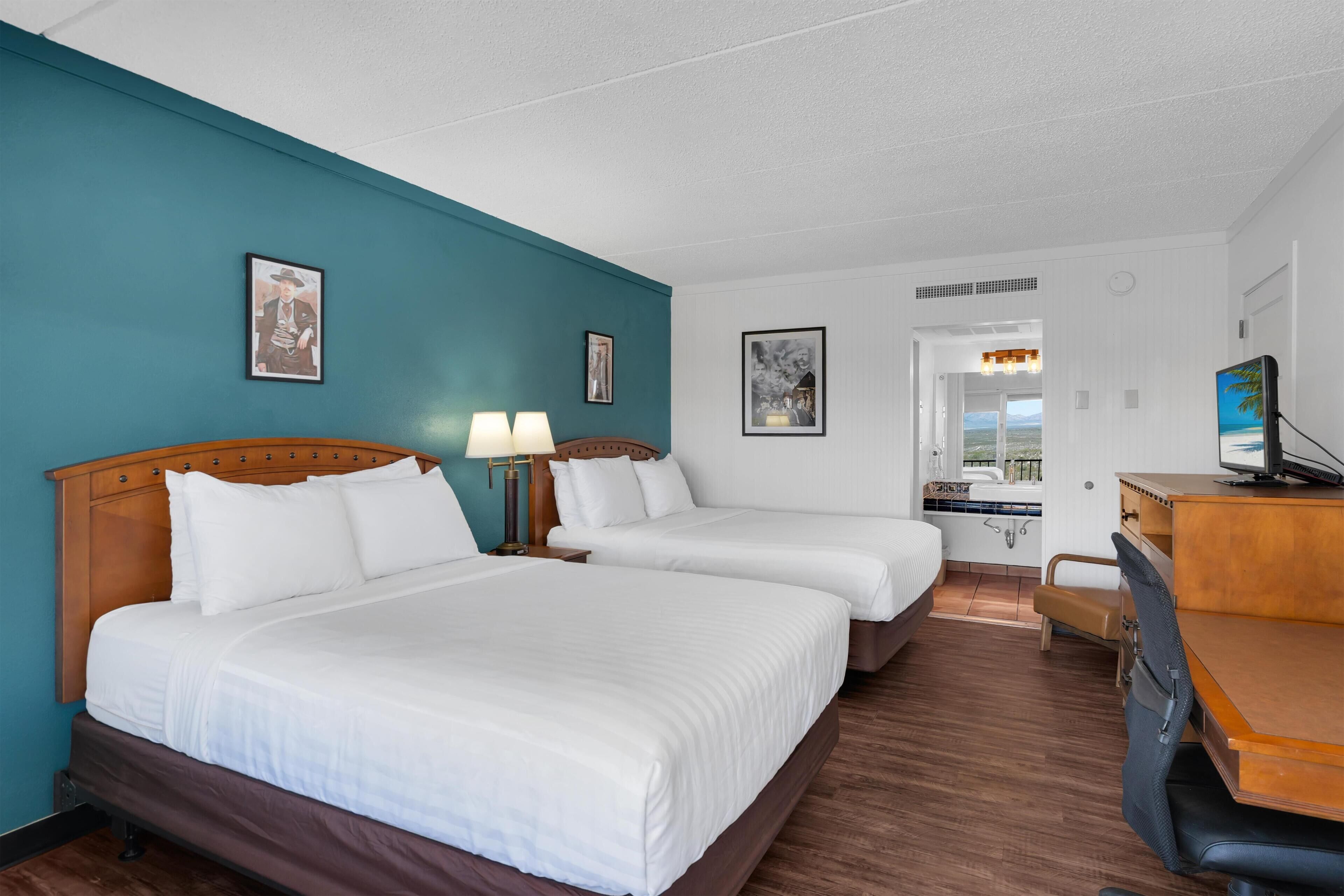 A hotel room with two beds, a desk, and a bathroom visible through an open door.