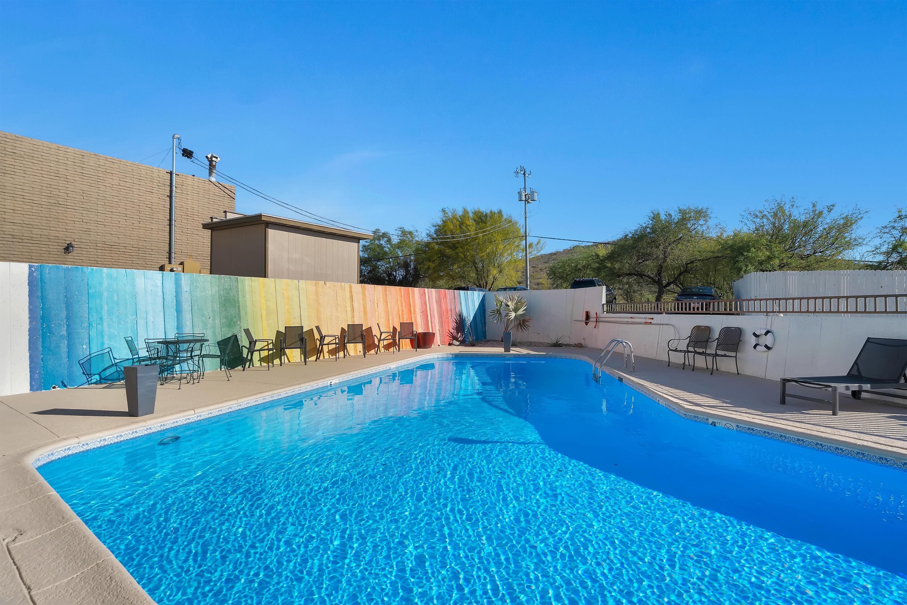 A swimming pool with lounge chairs and a colorful fence.