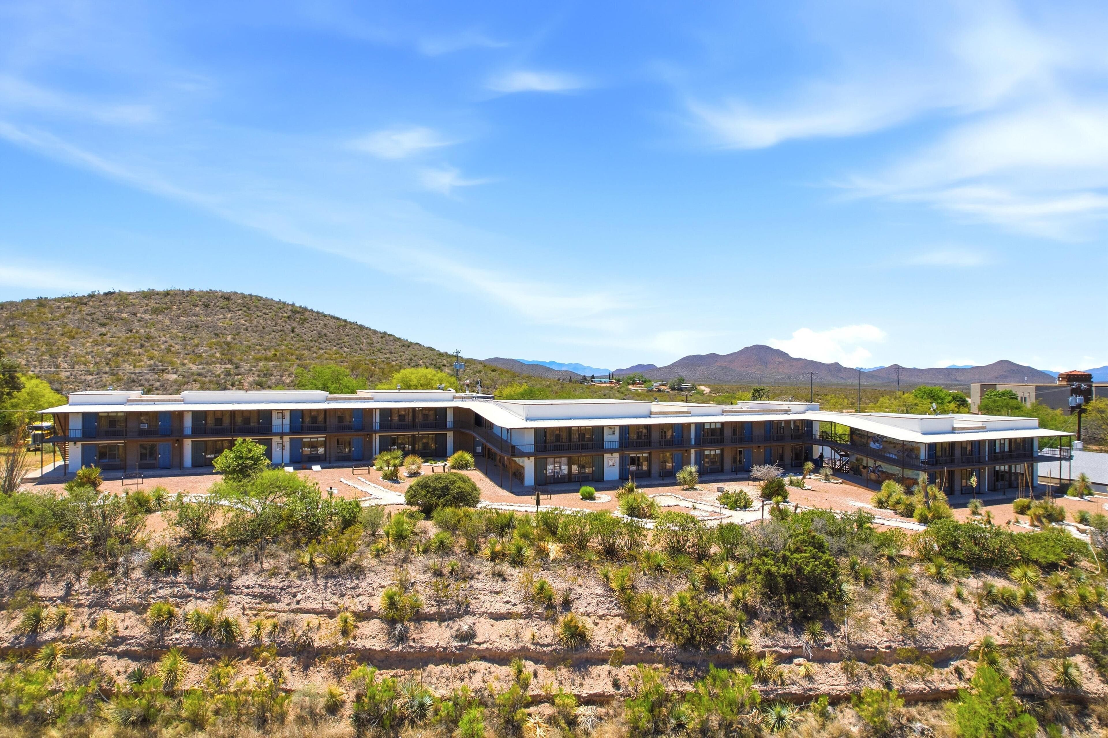 Un hotel moderno con tetto piatto, diverse camere e un paesaggio desertico con montagne sullo sfondo.