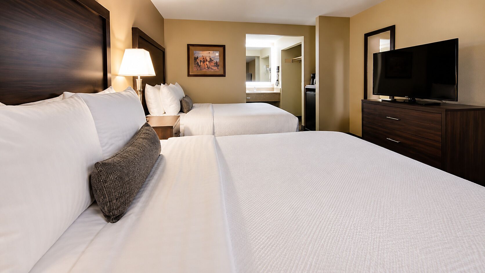 Une chambre d’hôtel avec deux lits, une télévision, un bureau et une salle de bain visible à travers une porte ouverte.