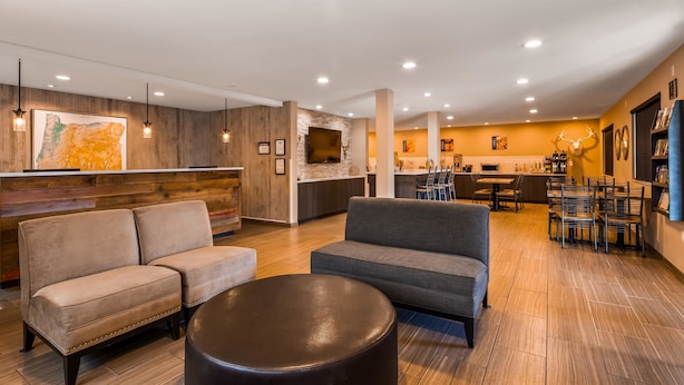 A modern hotel lobby with a wooden reception desk, sofas, a round coffee table, and a dining area with chairs and tables. - Best Western John Day Inn (John Day)