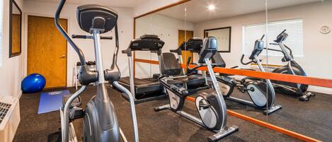 A gym with exercise equipment, a blue exercise ball, and a mirror reflecting the room.
