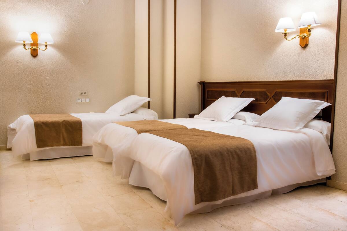Habitación de hotel con dos camas, paredes color beige y lámparas fijadas a la pared.