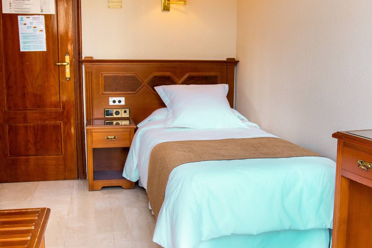 Una habitación de hotel con una cama de madera, una mesita de noche con un radio y un armario de madera.