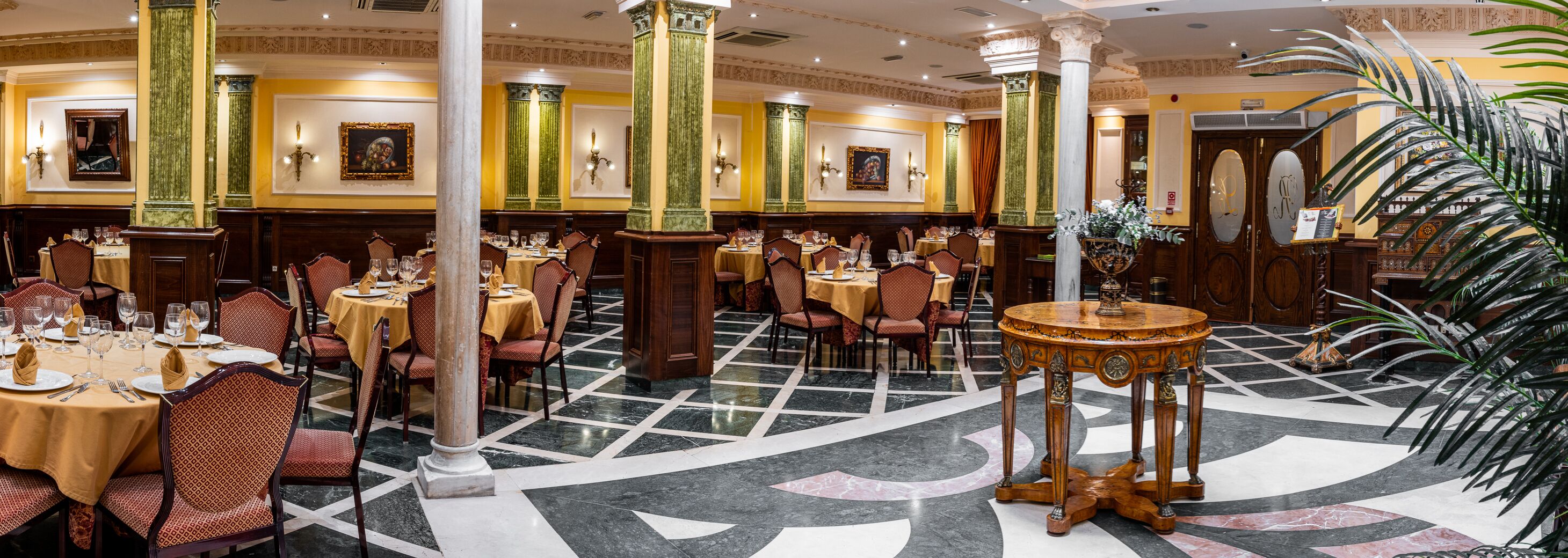 Un amplio comedor con varias mesas y sillas, columnas grandes y un diseño decorativo en el suelo.