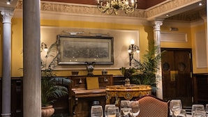 A dining area with a table set for a meal, a piano, and a large framed picture on the wall. - Hotel Reina Cristina (Granada)
