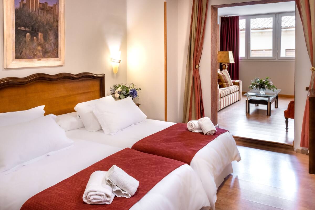 Habitación de hotel con dos camas, un cuadro en la pared, una mesa con flores y vistas al exterior.