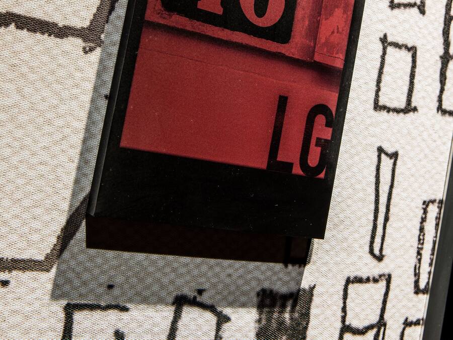 Eine Nahaufnahme eines roten und schwarzen Schildes mit der Nummer '46' und den Buchstaben 'LG' auf einem strukturierten Stoffhintergrund.