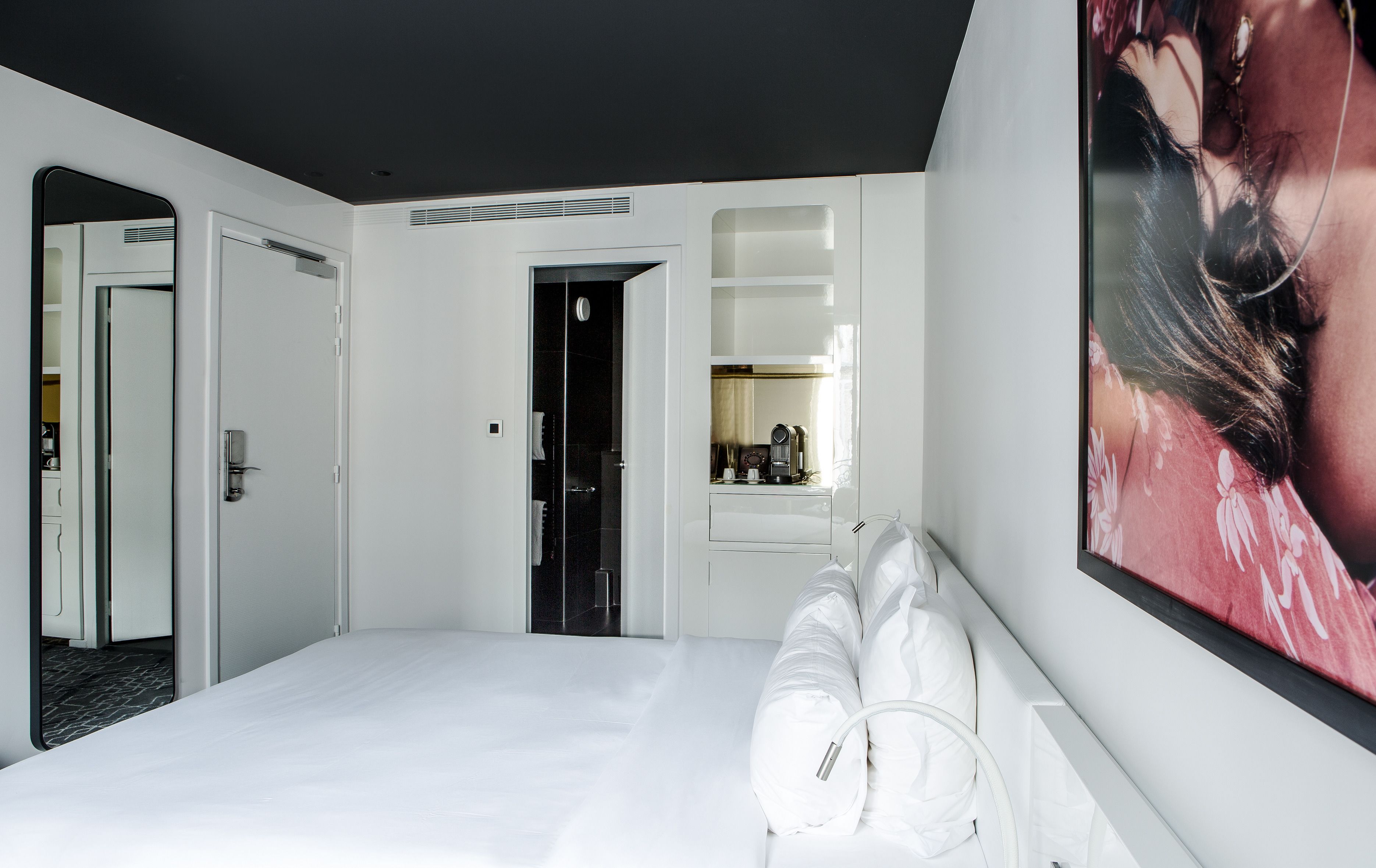 Ett modernt hotellrum med en stor säng, ett badrum med spegel och en väggmonterad TV.