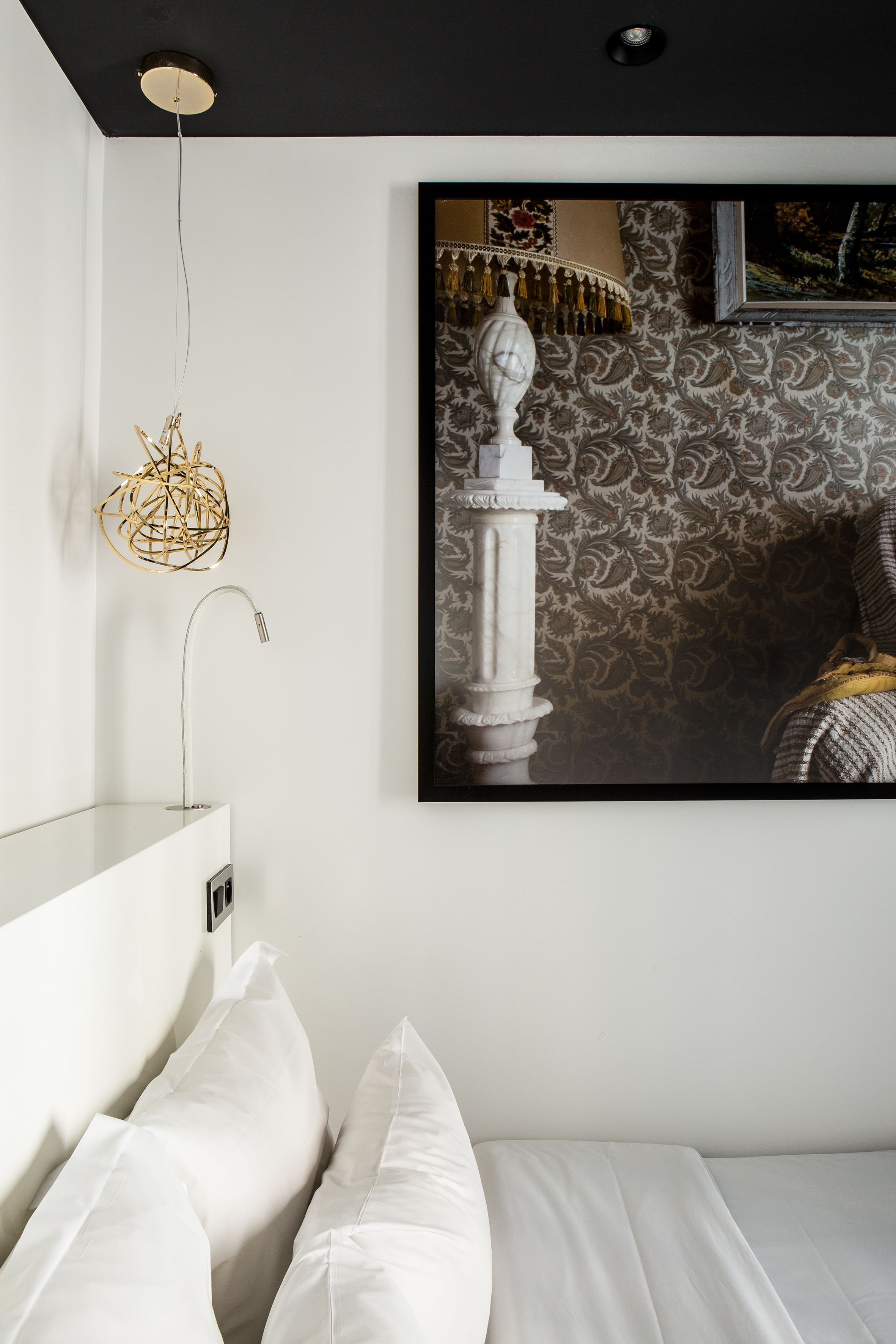 Une chambre à coucher comprenant un lit, un luminaire fixé au mur et une œuvre d’art encadrée représentant une statue.