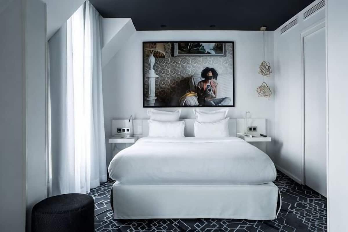 A modern hotel room with a large bed, bedside tables, a mirror, and a wall-mounted artwork.