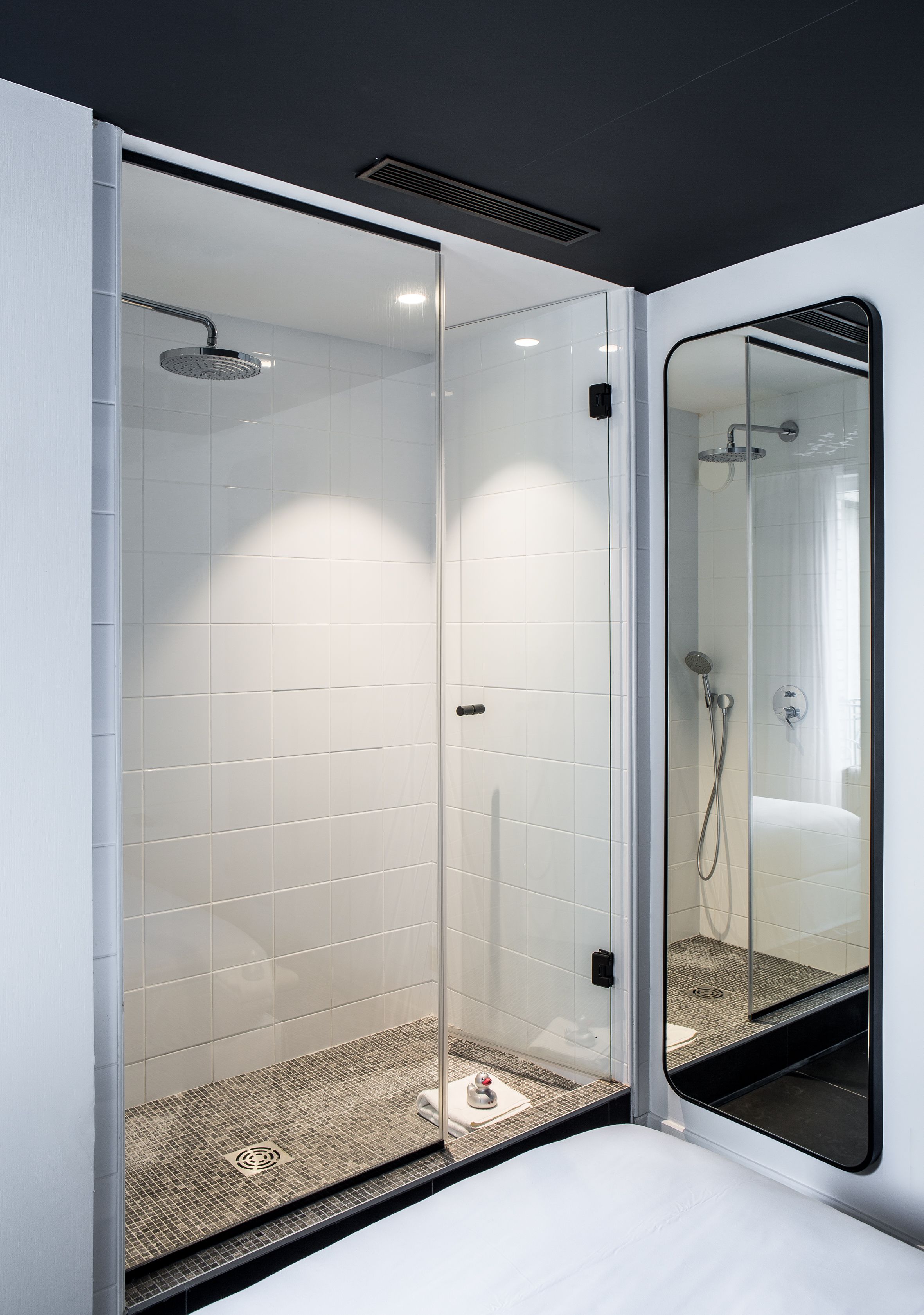 A modern bathroom with a glass-enclosed shower, white tiles, and a large mirror.