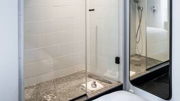 A modern bathroom with a glass-enclosed shower, white tiles, and a large mirror.