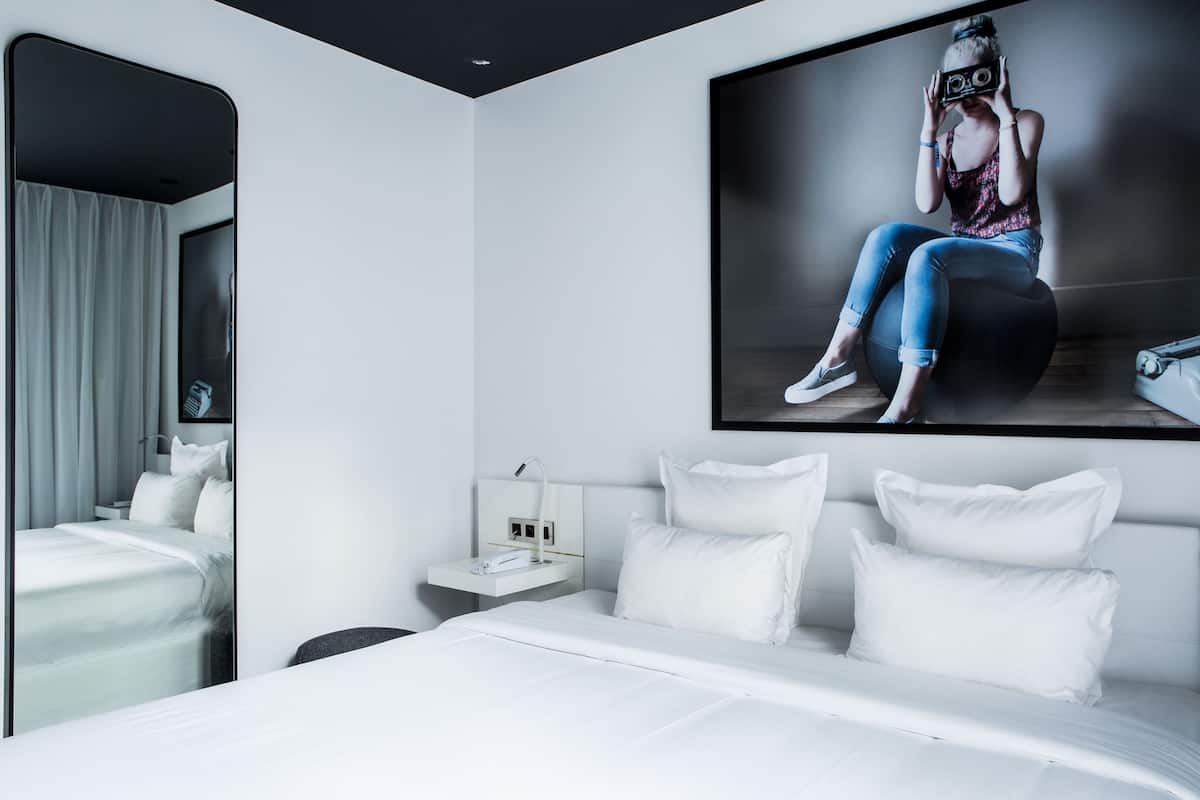 A modern hotel room with a large bed, a bedside table with a phone, and a wall-mounted TV.