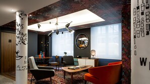 A modern interior with a central table, two chairs, a sofa, a mirror, and a decorative column with text. - Le General Hotel (Paris)