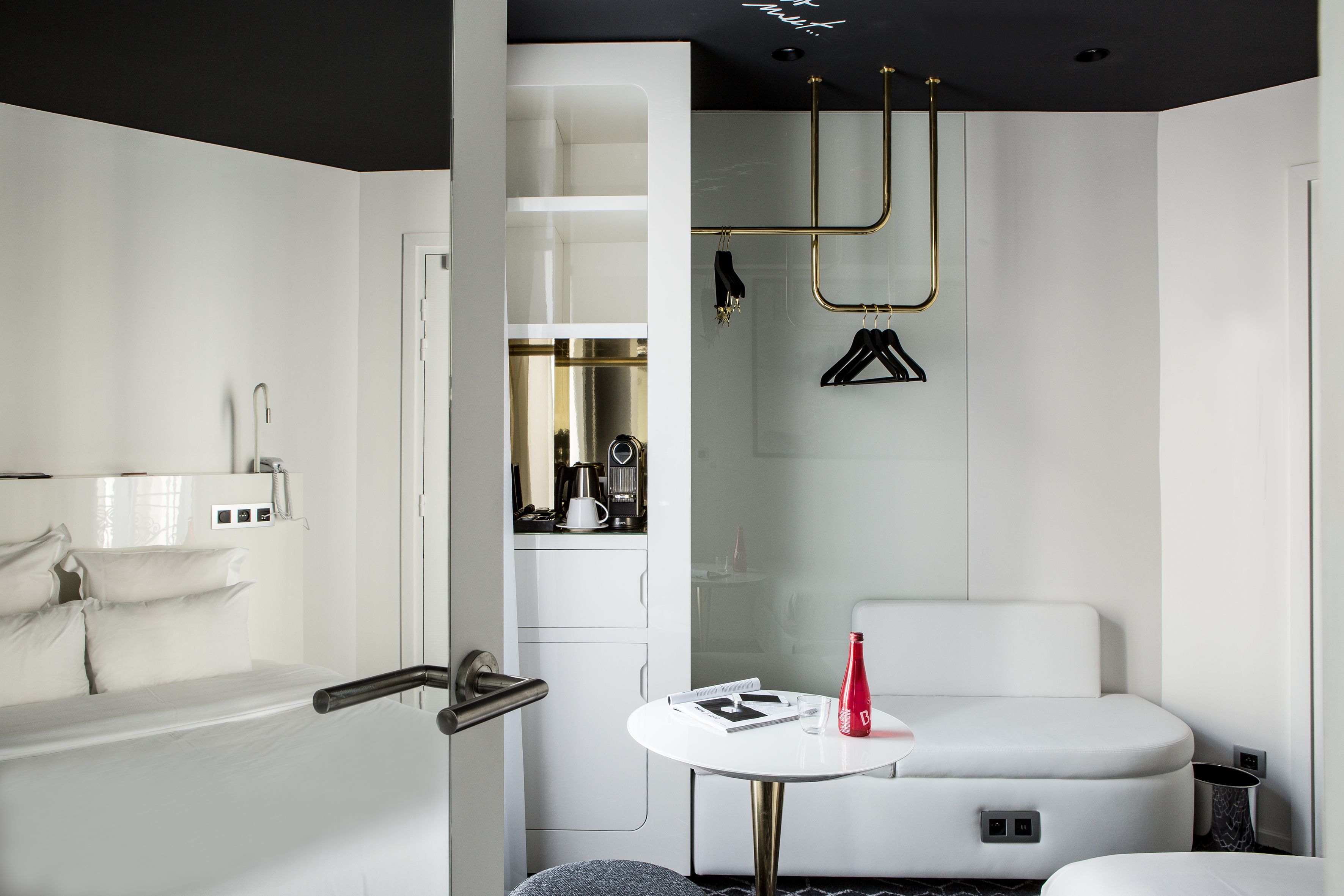 A modern bathroom with a white bathtub, a round table with a red bottle, and a white sofa.