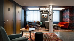 A modern hotel room with a wooden door, a round table with chairs, a colorful patterned carpet, and a large mirror on the wall. - Le General Hotel (Paris)