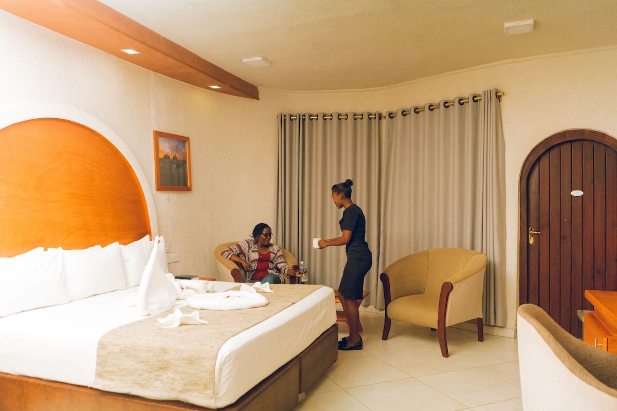 Quarto de hotel com uma cama grande, uma cadeira, uma porta de madeira e uma cortina.