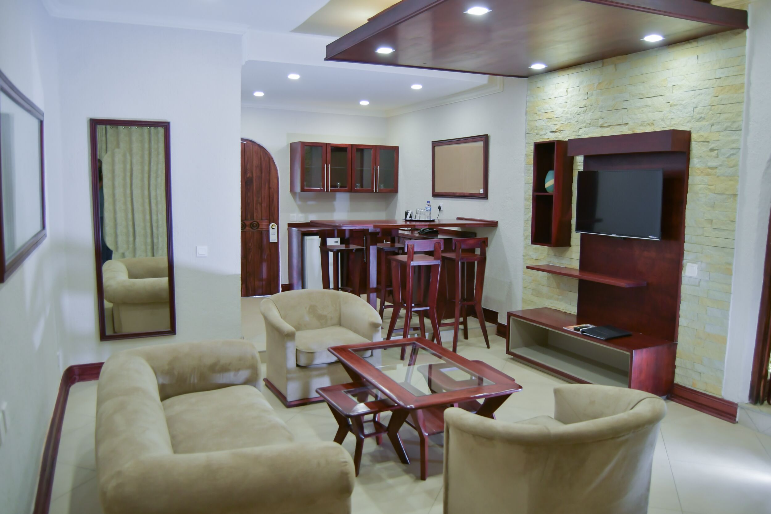 Una sala de estar con sofá, sillones, una mesa de centro, televisor, armarios de madera y una pared de piedra.