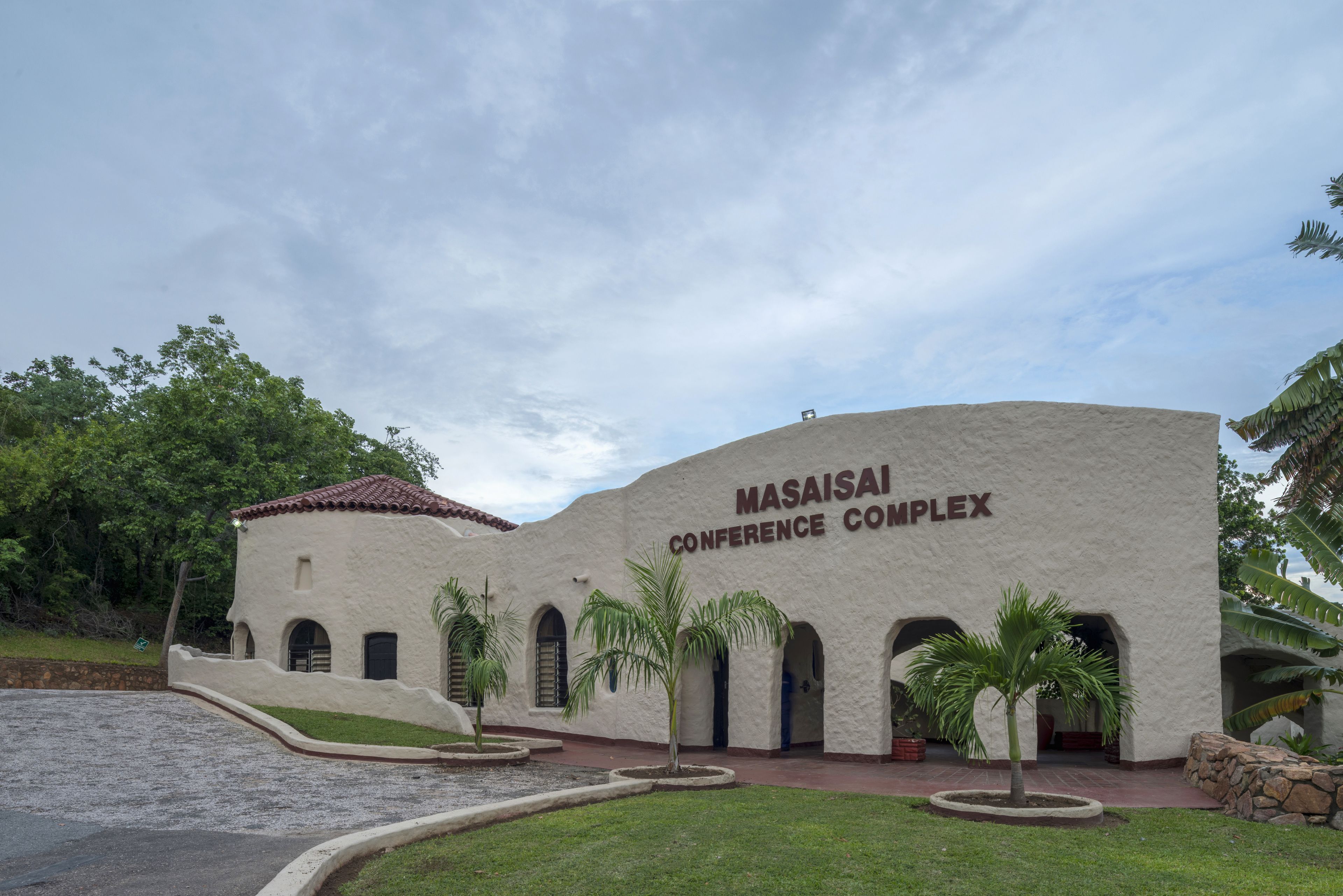 Le complexe de conférence Masaisi, avec sa façade blanche, ses fenêtres en arc de cercle et les palmiers qui l’entourent.