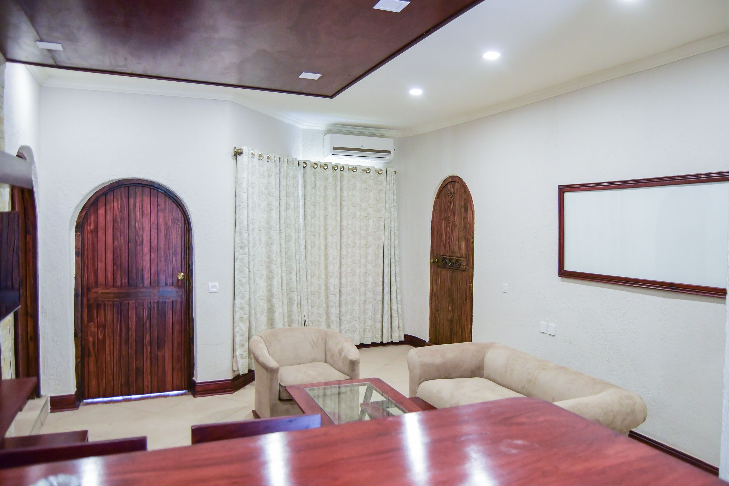 A living room with a wooden door, a sofa, a glass coffee table, and a wall-mounted TV.