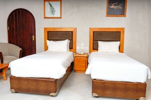 Habitación de hotel con dos camas, una puerta de madera, una silla y una mesita.