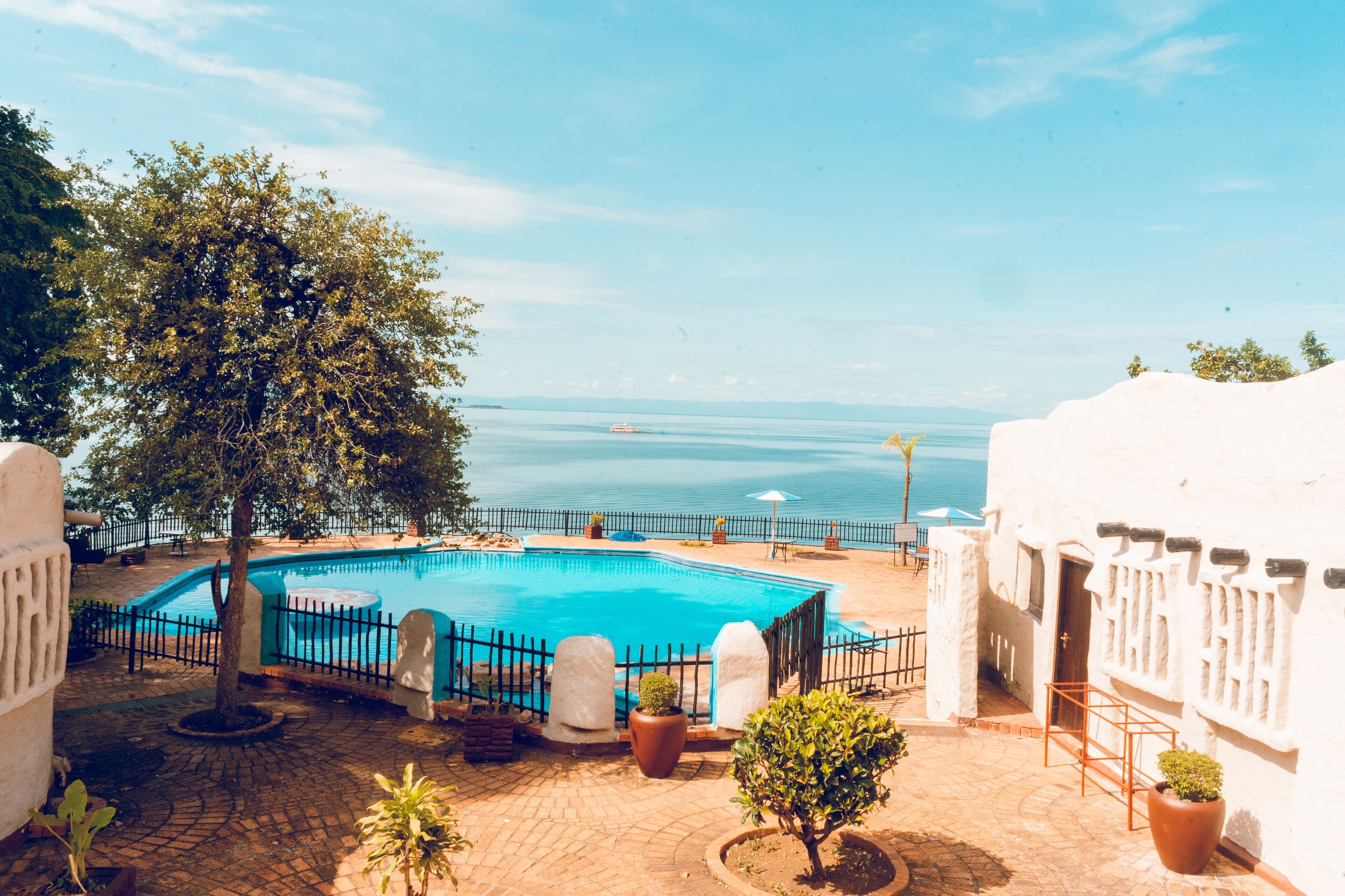 Zona de piscina con vista al mar, rodeada de plantas en macetas y un edificio blanco.