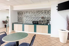 A modern kitchen with a tiled backsplash, a coffee machine, and a microwave. There is a dining area with a round table and chairs.