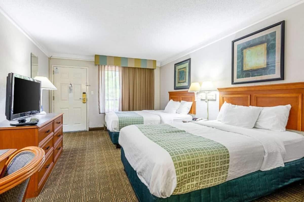 A hotel room with two beds, a television, a desk with a lamp, and a door.