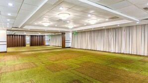 Une grande salle de conférence bien éclairée, dotée d’un tapis vert, de murs blancs et d’un mur recouvert d’un rideau.