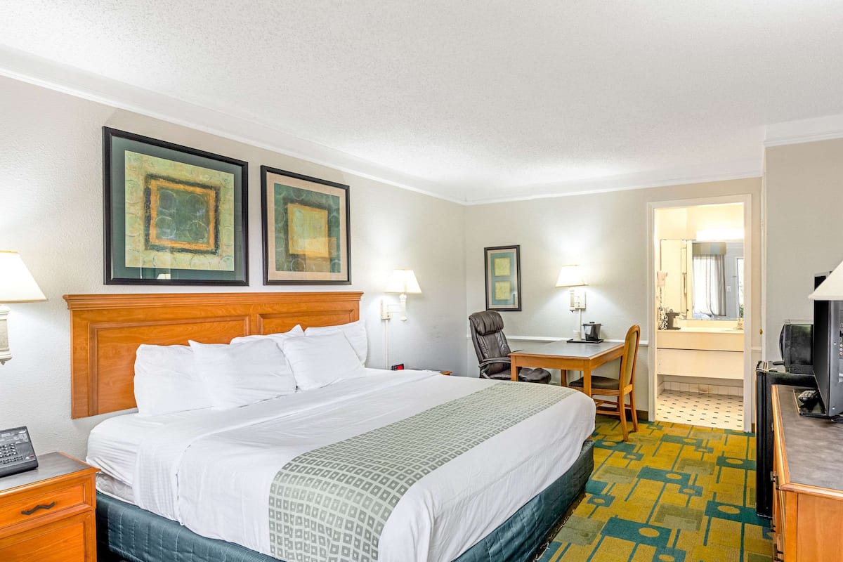 A hotel room with a large bed, a desk, a chair, a television, and two framed pictures on the wall.