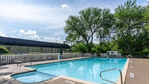 Une piscine rectangulaire avec un petit jacuzzi, entourée de chaises longues et d’une clôture en bois.
