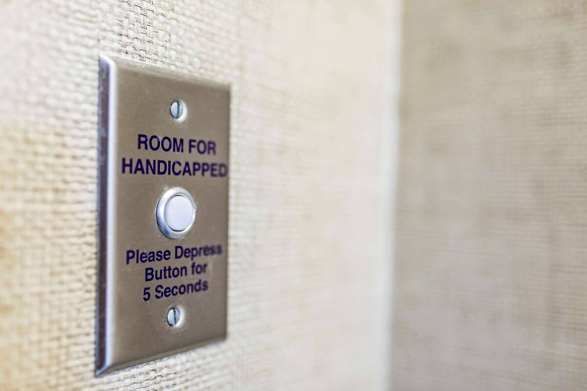 A sign indicating a room for handicapped individuals with a button to depress for 5 seconds.