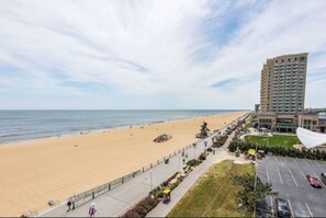 A beachside hotel with a long promenade, a parking lot, and a view of the ocean.