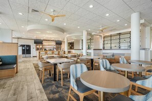 A spacious indoor area with multiple seating arrangements, including round tables and chairs, and a reception area with a counter and shelves.