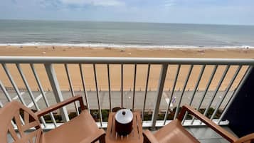 A balcony with two wooden chairs and a small table, overlooking a sandy beach and the ocean.