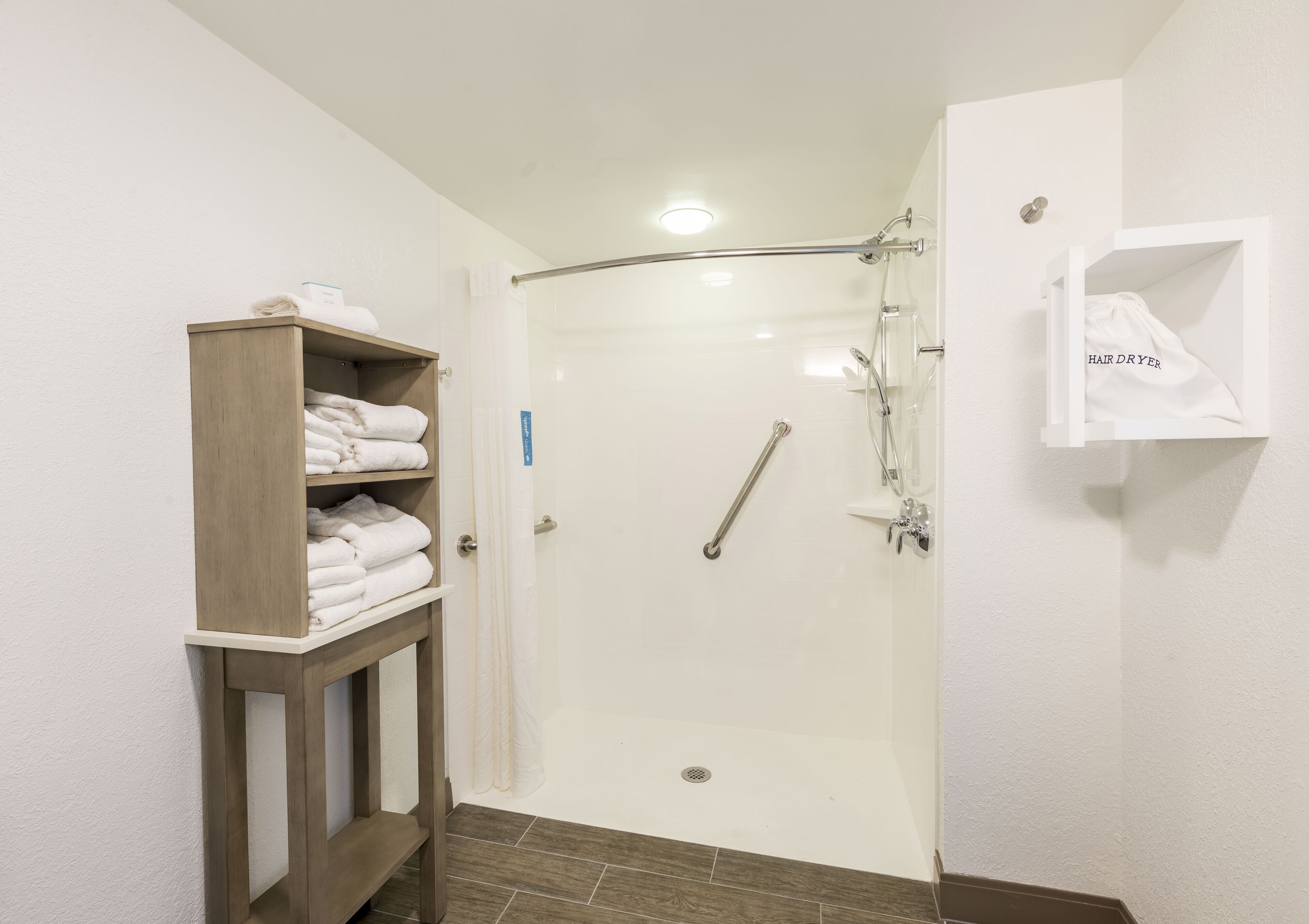 Ein modernes Badezimmer mit einer gläsernen Dusche, einem Holzhandtuchhalter und einem weißen Seifenspender.