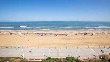 A wide beach with umbrellas and beach chairs, a clear sky, and the ocean in the background.
