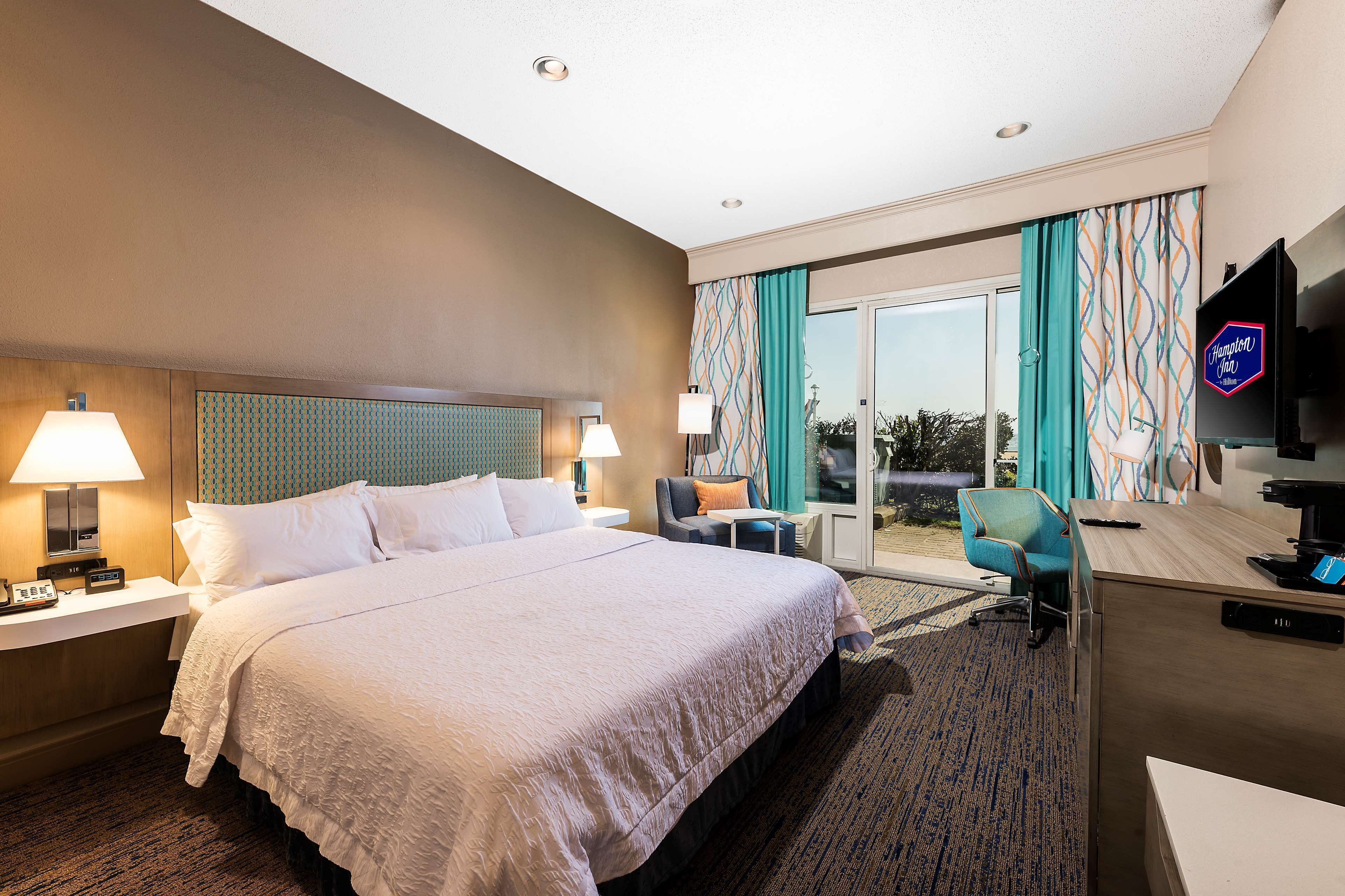 A hotel room with a large bed, two bedside tables with lamps, a desk with a computer, a chair, and a TV.