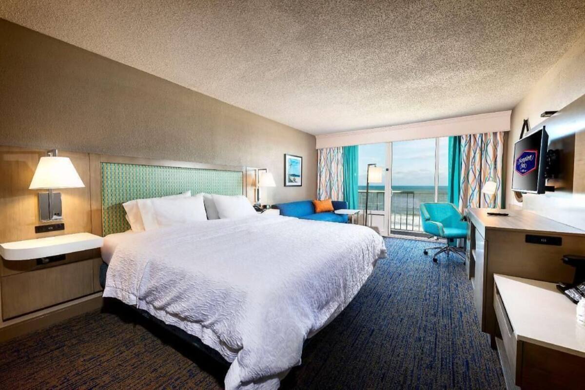 A hotel room with a large bed, a desk, a chair, and a TV.